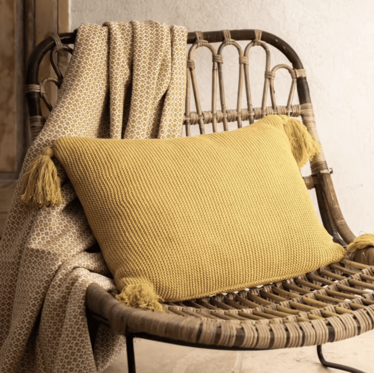 Un fauteuil naturel accompagné d'un coussin en nid d'abeille et d'un plaid en laine pour un confort optimal